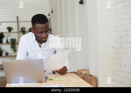 Glücklich fokussierter afroamerikanischer Mann, der einen Videoanruf mit Kundenpartnern führt. Der junge schwarze Mann nutzt im modernen Büro einen Laptop. Stockfoto