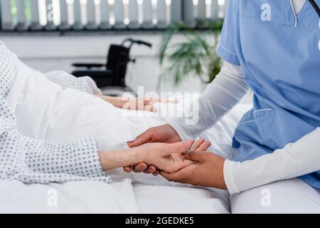 Beschnittene Ansicht einer afroamerikanischen Krankenschwester, die den Puls an der Hand eines älteren Patienten überprüft Stockfoto