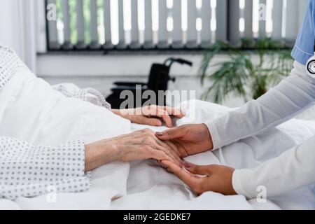 Beschnittene Ansicht einer afroamerikanischen Krankenschwester, die die Hand eines älteren Patienten hält Stockfoto