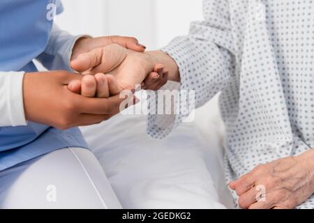 Beschnittene Ansicht einer afroamerikanischen Krankenschwester, die den Druck auf die Hand eines älteren Patienten überprüft Stockfoto