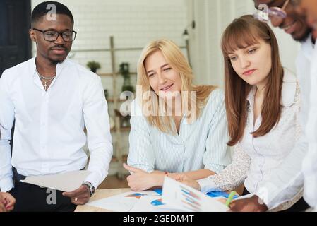 Ein multinationales, positives Unternehmen von Menschen arbeitet im Büro und schaut sich Arbeitsunterlagen an. Stockfoto