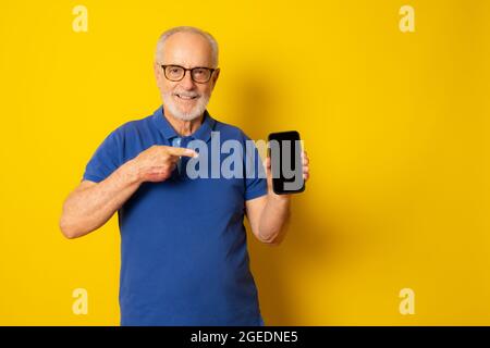Lifestyle, Tehnologie und Old People Konzept: Schöner alter grauhaariger Mann, gekleidet in smarten Casual Style mit einem Smartphone und lächelnd über gelbem Bac Stockfoto