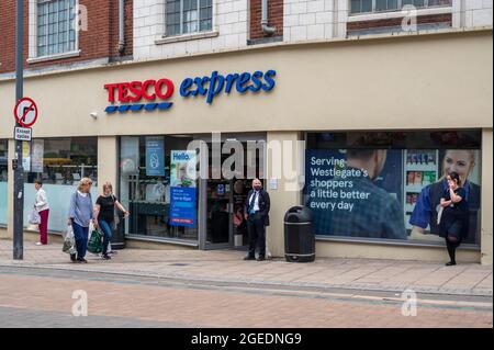 Tesco Express Westlegate Norwich mit Tesco Sicherheitsfrau, die draußen mit einer Gesichtsmask steht, und Einkäufern, die vorbeilaufen Stockfoto