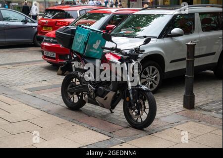 Ein Honda Motorrad mit einer großen Deliveroo-Box auf der Rückseite, das in der Nähe eines Macdonalds Restaurants im Stadtzentrum von Norwich geparkt ist Stockfoto