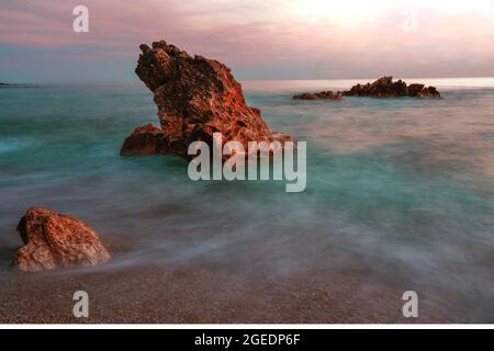 Langzeitbelichtung bei Sonnenuntergang mit Bewegungsunschärfe und Felsen Stockfoto