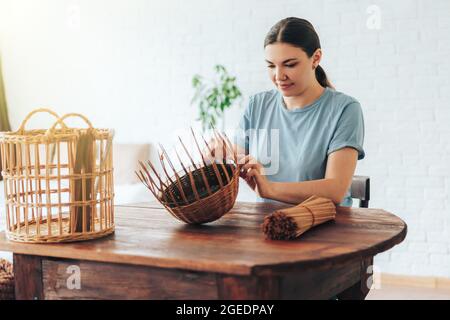 Frau webt Korb mit Papierröhrchen auf Holztisch. Stockfoto