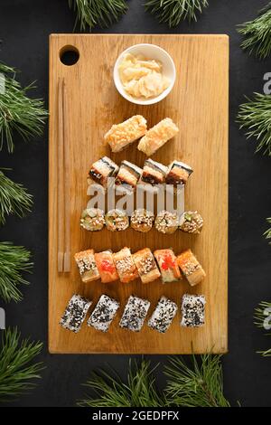 Sushi-Set serviert als Weihnachtsbaum auf Holzschneidebrett auf schwarzem Hintergrund. Blick von oben. Vertikales Format. Stockfoto