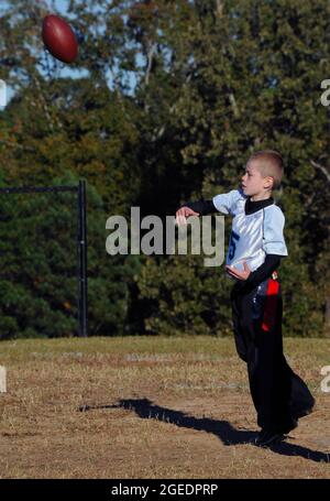 Fußball wird von einem Jungen Quarterback während eines organisierten Flaggen-Fußballspiels geworfen. Er trägt ein Trikot und Fahnen. Fußball ist in Bewegung und fliegt t Stockfoto