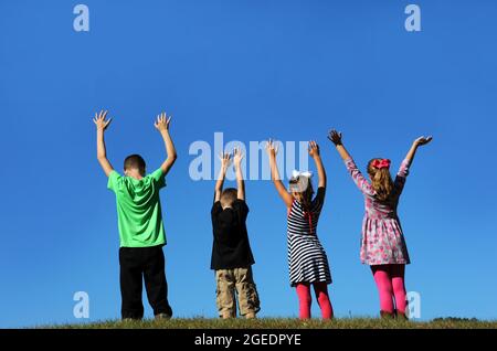 Vier Kinder heben ihre Hände zum Himmel und werden von einem leuchtend blauen Himmel umrahmt. Stockfoto