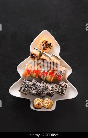 Sushi-Set serviert in Teller als Weihnachtsbaum mit festlicher Dekoration auf schwarzem Hintergrund. Blick von oben. Stockfoto