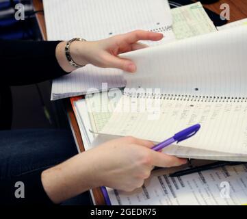 Die Lehrerin sitzt in ihrem Klassenzimmer und bewertet Hausaufgaben. Sie blättert Seiten im Notizbuch der Studenten. Stockfoto