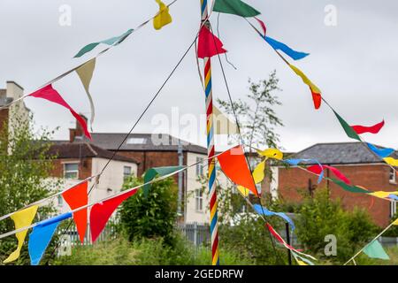 Ein knallfarbener Fahnenmast und dreieckige Flaggen stehen im Kontrast zu den gedämpften Farben der langweiligen Stadtlandschaft dahinter. Stockfoto