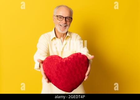 Älterer Mann mit herzförmigem Kissen auf gelbem Hintergrund. Stockfoto