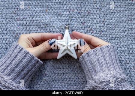Weibliche Hände in Strickpullover mit weißem Christbaumstern und schöner Maniküre - dunkelgrau blau glitzernde Nägel auf gestricktem Hintergrund Stockfoto