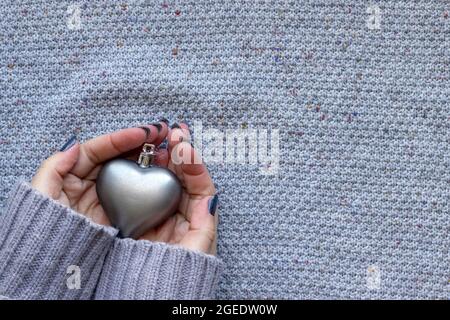 Weibliche Hände in Strickpullover mit mattem Herz und schöner Maniküre - dunkelgrau blau glitzernde Nägel auf gestricktem Hintergrund mit Kopierfläche Stockfoto