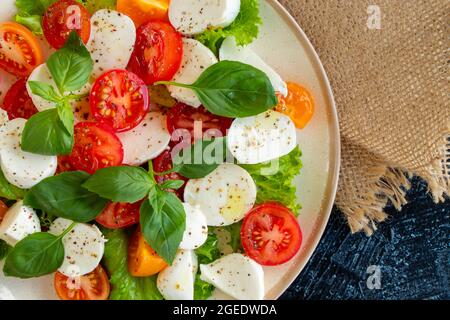 Nahaufnahme Mozzarella, Tomaten Basilikumblatt auf einer Gabel auf einem Hintergrund von Gemüsesalat mit Käse. Draufsicht. Weichfokus Stockfoto