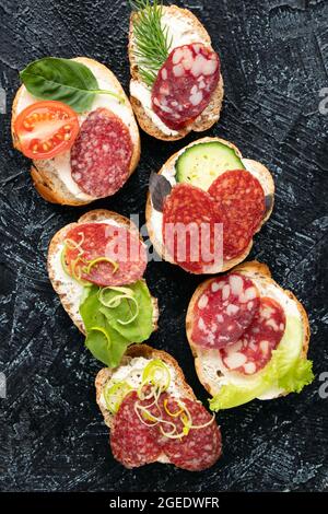 Arten Sandwiches oder Snacks mit verschiedenen Sorten Wurst und Gemüse auf schwarzem Hintergrund. Weicher Fokus. Draufsicht. Vertikale flache Lage Stockfoto