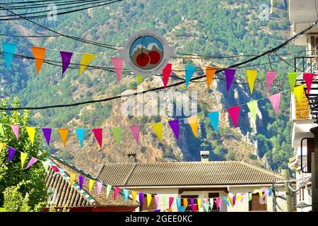 Güéjar-Sierra (Granada), Spanien; 19. August 2021: Eine Straße in Gúéjar-Sierra (Spanien), geschmückt mit farbigen Bannern zur Feier des Kirschenfestes Stockfoto