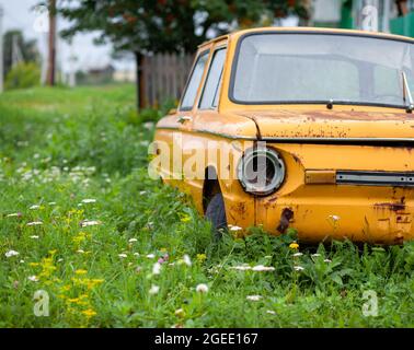 Altes gelbes Wrackauto im Vintage-Stil. Verlassene rostige gelbe Auto. Nahaufnahme der Scheinwerfer der Vorderansicht eines rostigen, gebrochenen, verlassenen Autos Stockfoto