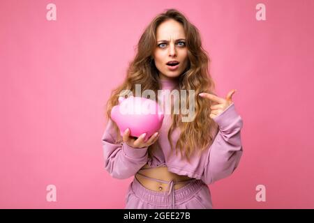 Portrait of Amazes schockiert überrascht junge charmante schöne Frau mit welligen langen blonden Haaren mit aufrichtigen Emotionen tragen stilvolle rosa Hoodie Stockfoto