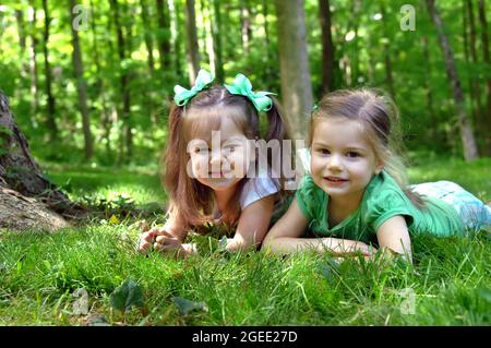 Zwei Schwestern lagen auf dem Gras ihres Hofes. Jede Schwester hat einen anderen Ausdruck auf ihren Gesichtern. Eine Schwester sieht uneinlich aus und die andere süß und s Stockfoto