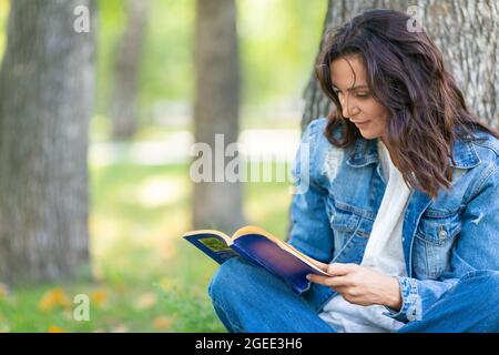 Nahaufnahme einer 40-jährigen Frau, die im Park ein Buch liest. Sie macht eine Pause von der Arbeit am Computer und ständig online. Digitale Entgiftung Stockfoto