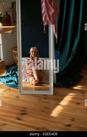 Spiegelung des lächelnden jungen Hörens von Musik mit Kopfhörern und Mobiltelefon im Schlafzimmer Stockfoto