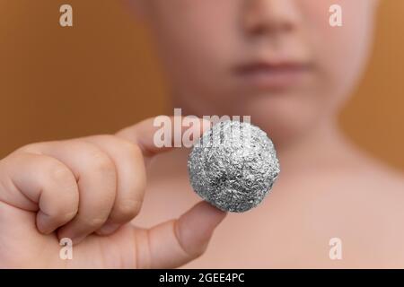 Junger Junge, der eine Aluminiumfolie in Form einer Kugel hält Stockfoto
