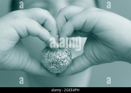 Junger Junge, der eine Aluminiumfolie in Form einer Kugel hält Stockfoto