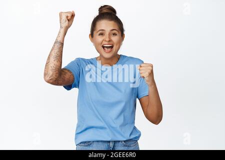 Aufgeregt Mädchen, die für Team, beobachten Sportspiel und Chanten mit Faust Pumpe, Schreien vor Freude, stehen begeistert vor weißem Hintergrund Stockfoto