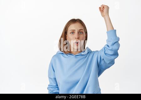 Go Team. Junge blonde Mädchenaktivistin, die die Faust hochhebt, die Menschenrechte bekämpft, vereint bleibt, chantet, an der lgbtq Pride Parade teilnimmt, im Hoodie steht Stockfoto