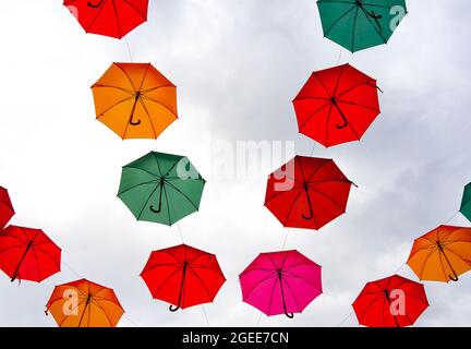 Aufnahmen von bunten Regenschirmen, die über der Straße gegen den bewölkten Himmel hängen Stockfoto