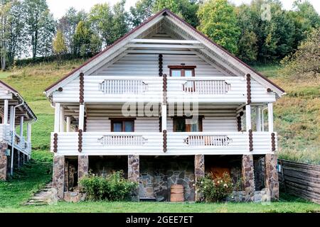 Weißes Blockhaus-Chalet auf Berghügeln. Schönes zweistöckiges Holzhaus im Sommer auf der Seite des Berges. Außenansicht des Hauses in den Bergen Stockfoto