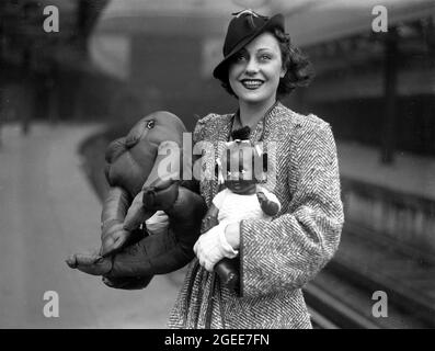 Hübsche Frau mit einer schwarzen Topsy-Puppe und einem weichen Spielzeug-Frosch in Victoria Station, London, 1930 Stockfoto