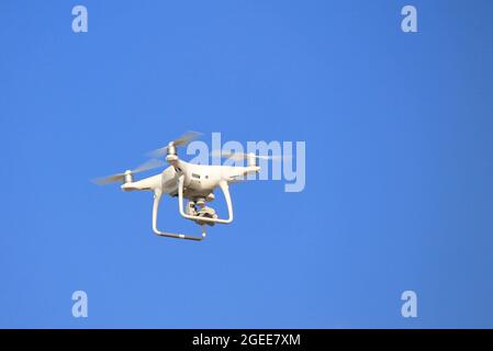 Weiße Drohne, mit einer Kamera, fliegt gegen einen blauen wolkenlosen Himmel. Quadrocopter, unbemanntes Luftfahrzeug im Flug Stockfoto