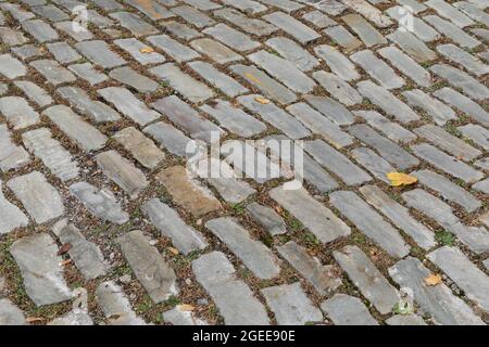 Straße gepflastert mit grauen Steinblöcken, Gras und Schutt in den Rändern, horizontaler Aspekt Stockfoto