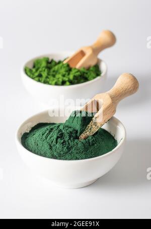 Bio-Algen Chlorella und Spirulina in Pulverform in weißen Schalen mit Holzschaufeln auf weißem Hintergrund. Stockfoto