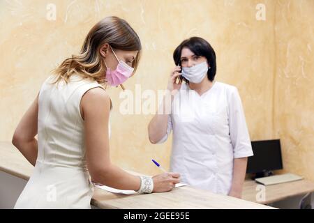 Kunde unterzeichnet Papier an der Rezeption in Gesichtsmaske in der medizinischen Klinik Stockfoto