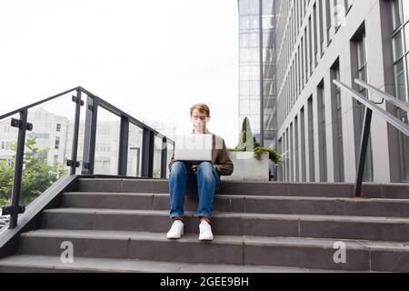 Mann, der an einem Laptop arbeitet und auf der Treppe des Business Centers sitzt Stockfoto
