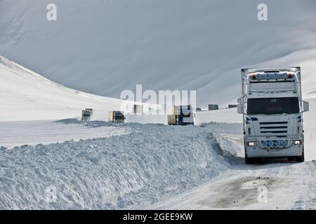 Lastwagen fahren auf der schneebedeckten Straße Nr. 1 in Island, die vom Oxnadalsheidi-Pass herunterkommt Stockfoto
