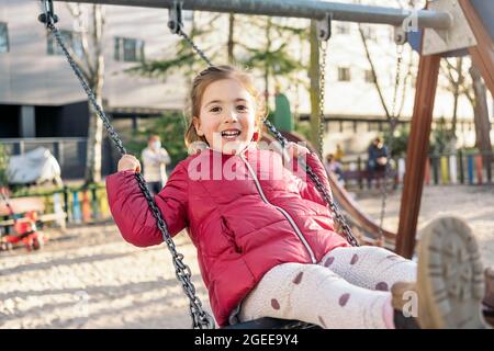 Ein schulpflichtig lächelndes Mädchen, das auf der Fahrt fröhlich lächelt Schaukeln im Park Stockfoto