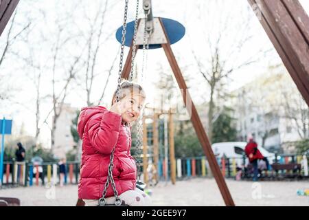 Ein schulpflichtig lächelndes Mädchen, das auf der Fahrt fröhlich lächelt Schaukeln im Park Stockfoto