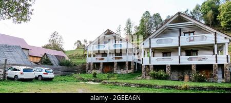 Zwei schöne weiße Holz-Chalet-Hütten Häuser und 2 weiße Autos in Bergdorf schöne ländliche Landschaft. Modernes Leben in der Natur Sommerhaus Stockfoto