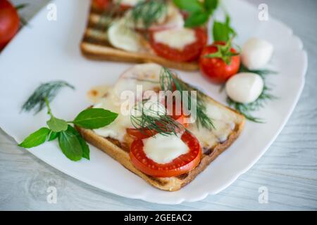 Gebratener heißer Toast mit Mozzarella und Tomaten auf einem Teller auf einem Holztisch Stockfoto