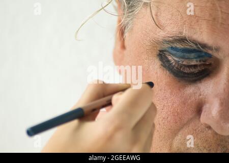 Hand eines Mädchens, das die Augen eines ernsthaften reifen Mannes mit Kosmetik auf weißem Hintergrund malt Stockfoto