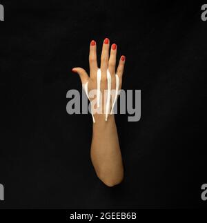 Weiße Farbstreifen tropfen über die offene Hand auf schwarzen Hintergrund. Stockfoto