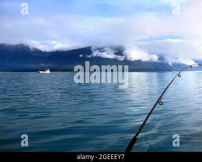 Die wunderschöne Bucht von Valdez am frühen Morgen bietet friedliche Angelmöglichkeiten. Wolken hängen tief über dem Chugach-Gebirge, und ein Schiff gleitet über das Wasser. Stockfoto