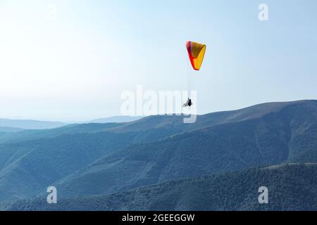 Der Mann auf dem Gleitschirm fliegt mit einem Fallschirm über die Berge hinter dem blauen Himmel. Extremsport und Freiheit Stockfoto