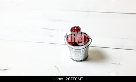 Süße Kirschen in einem kleinen Eimer auf Holzgrund, Nahaufnahme. Frische reife Süßkirschen in einem Eimer mit Wassertröpfchen Stockfoto
