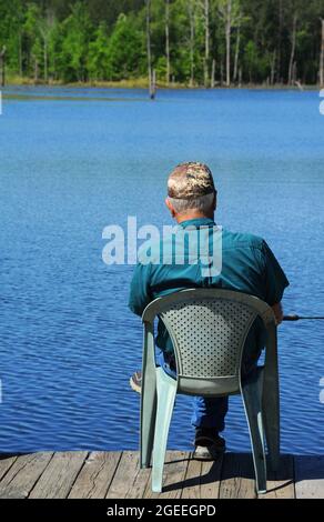 Ein älteres Männchen sitzt am Rande eines hölzernen Docks über dem Cooty Lake im Süden von Arkansas. Er fischt Brassen und wartet geduldig auf einen Bissen. Stockfoto